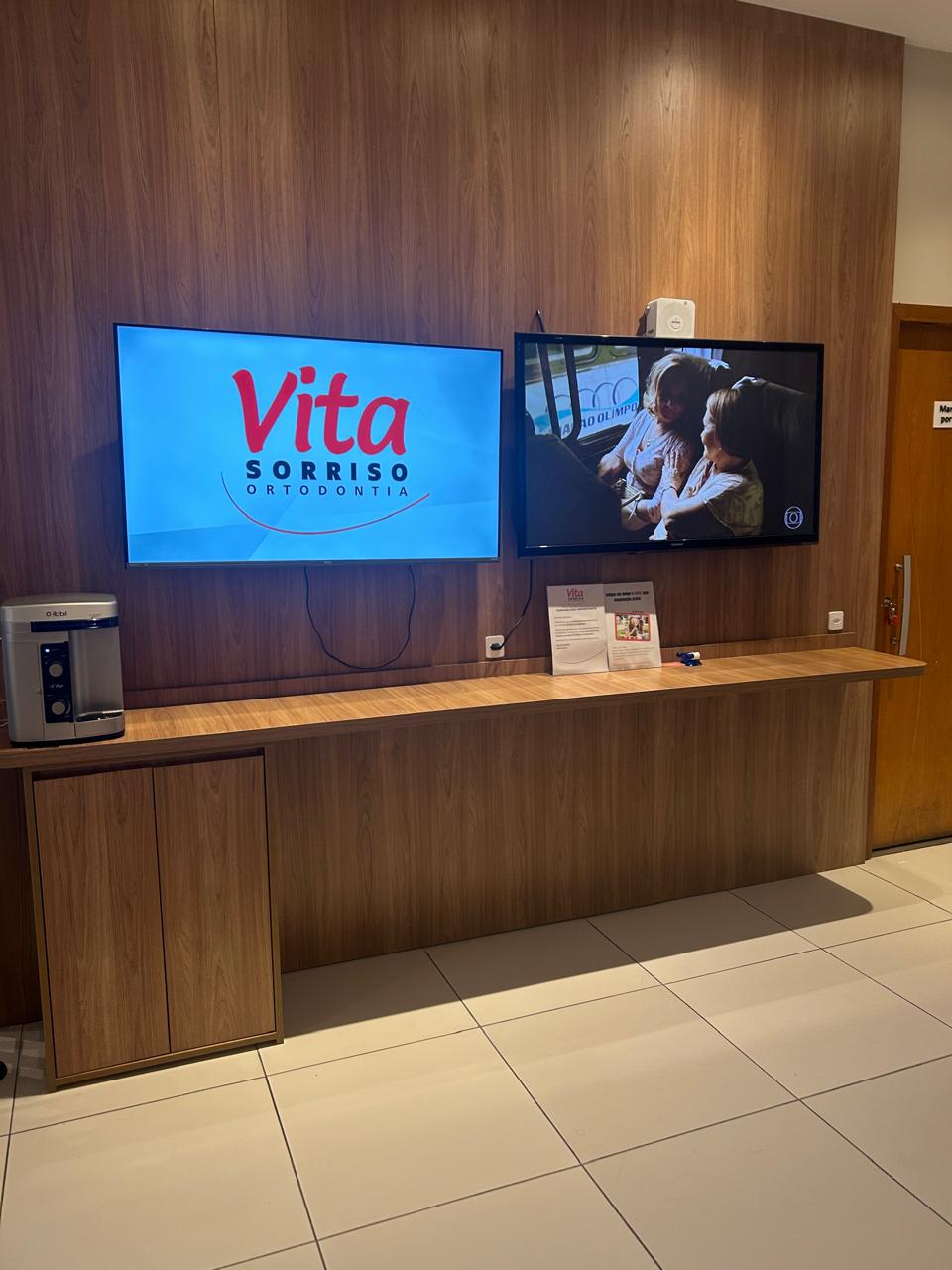 Sala de espera da Vita Sorriso com painel de madeira e TV com o logo da clínica